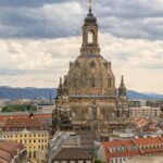 A stunning aerial view of the Frauenkirche in Dresden, showcasing Baroque architecture amidst city buildings under a cloudy sky.